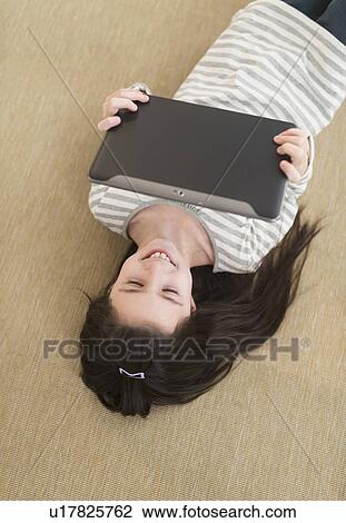 Stock Image - Girl (8-9) lying on floor using tablet pc. Fotosearch