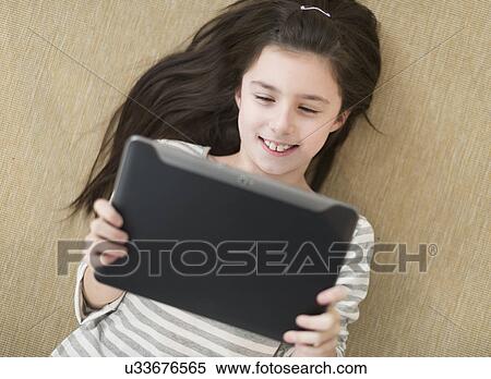 Stock Photography - Girl (8-9) lying on floor using tablet pc. Fotosearch