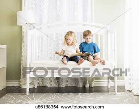 Picture - Girls (6-7) and boy (8-9) sitting on sofa and reading book. Fotosearch
