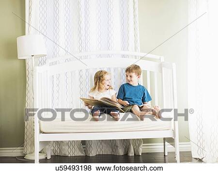 Stock Photo - Girls (6-7) and boy (8-9) sitting on sofa and reading book. Fotosearch