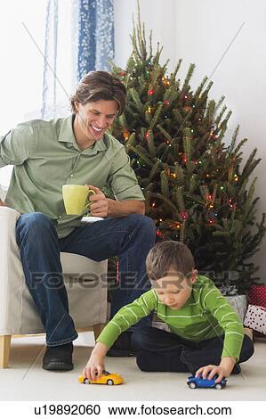 Stock Image - Man drinking tea and boy (6-7) playing with cars. Fotosearch