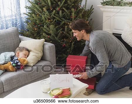 Man giving presents under Christmas tree while his son (6-7) sleeping View Large Photo Image Stock Photograph - Man giving presents under Christmas tree while his son (6-7) sleeping. Fotosearch