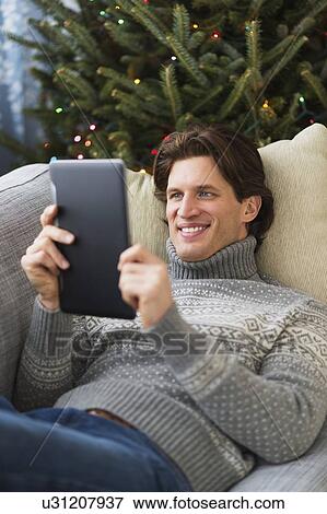 Stock Photo - Man lying on sofa and using tablet. Fotosearch