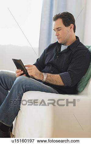 Man sitting on sofa looking at digital tablet View Large Photo Image Stock Photo - Man sitting on sofa looking at digital tablet. Fotosearch