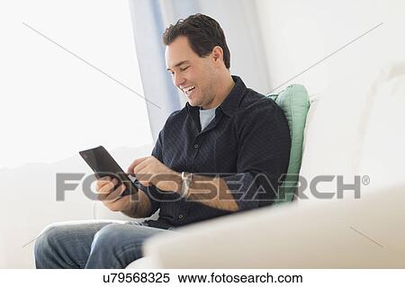 Man sitting on sofa looking at digital tablet View Large Photo Image Stock Photography - Man sitting on sofa looking at digital tablet. Fotosearch