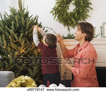 Man with kid (6-7) decorating Christmas tree View Large Photo Image Stock Photo - Man with kid (6-7) decorating Christmas tree. Fotosearch