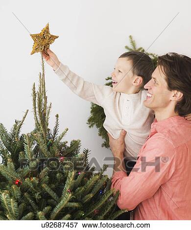 Stock Photo - Man with kid (6-7) decorating Christmas tree. Fotosearch