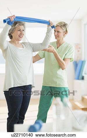 Stock Image - Mature woman exercising with personal trainer. Fotosearch