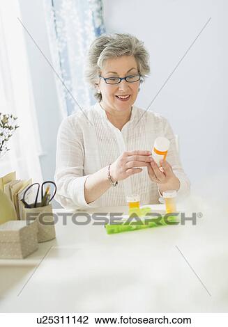 Stock Image - Mature woman reading labels on medicine bottle. Fotosearch