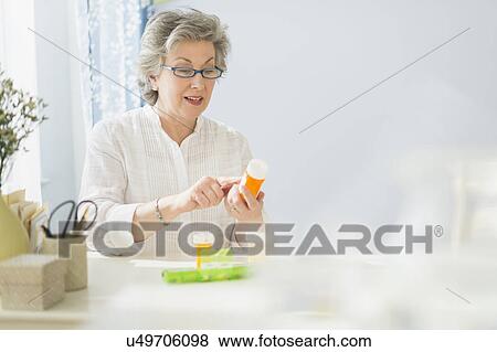 Stock Photo - Mature woman reading labels on medicine bottle. Fotosearch