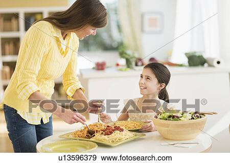 Stock Photo - Mother and daughter (8-9) eating pasta. Fotosearch