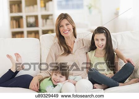 Stock Photo - Mother and daughters (4-5, 8-9) sitting on sofa. Fotosearch
