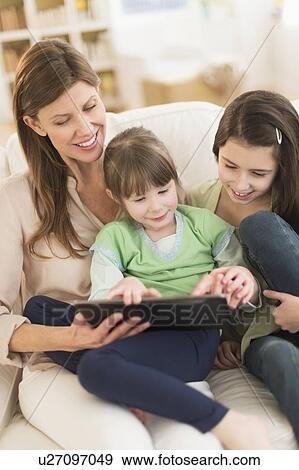 Stock Photo - Mother and daughters (4-5, 8-9) using tablet pc. Fotosearch