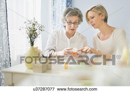 Nurse and mature woman reading labels on medicine bottle View Large Photo Image Stock Photo - Nurse and mature woman reading labels on medicine bottle. Fotosearch
