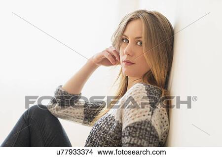 Picture - Portrait of attractive young woman sitting by wall. Fotosearch