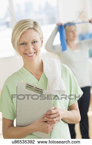 Stock Image - Portrait of personal trainer, mature woman exercising in background. Fotosearch