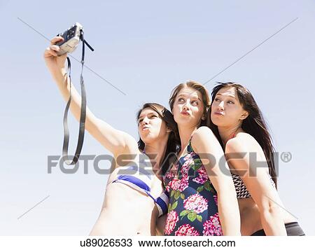Stock Image - Portrait of three women photographing themselves. Fotosearch