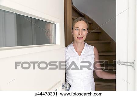Stock Image - Portrait of woman opening door. Fotosearch