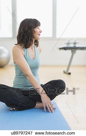 Stock Photo - Portrait of woman sitting on mat in gym. Fotosearch