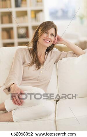 Stock Image - Portrait of woman sitting on sofa. Fotosearch