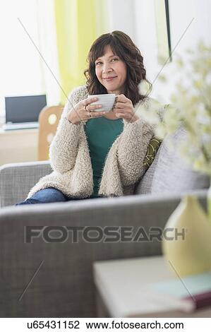 Portrait of woman sitting on sofa holding hot drink View Large Photo Image Stock Image - Portrait of woman sitting on sofa holding hot drink. Fotosearch
