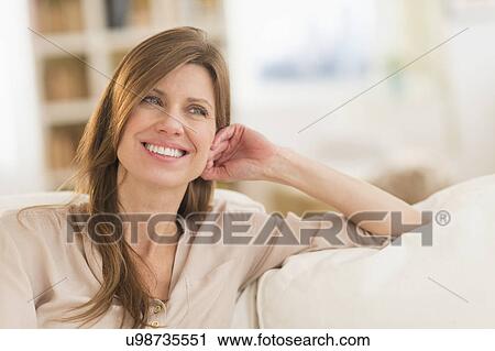 Stock Image - Portrait of woman sitting on sofa. Fotosearch