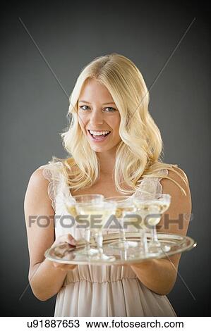 Stock Image - Portrait of young woman holding tray with champagne. Fotosearch