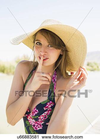 Stock Image - Portrait of young woman wearing sun hat on beach. Fotosearch