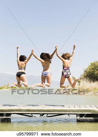 Stock Image - Three women jumping into lake. Fotosearch