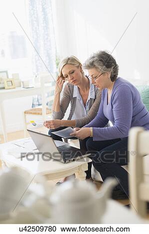 Stock Image - Two mature women paying bills via internet. Fotosearch