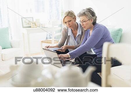 Stock Image - Two mature women paying bills via internet. Fotosearch