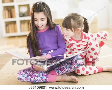 Stock Image - Two sisters (4-5, 8-9) reading picture book. Fotosearch