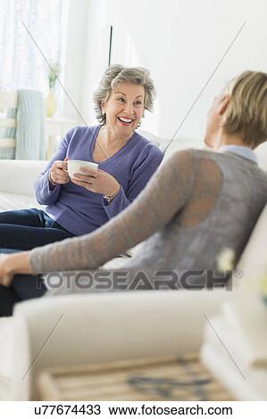Stock Image - Two women sitting on coach talking. Fotosearch