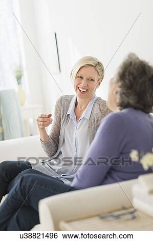 Stock Photograph - Two women sitting on coach talking. Fotosearch