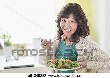 Stock Image - Woman eating salad at home. Fotosearch