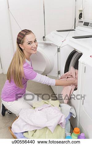 Stock Image - Woman loading laundry into washing machine. Fotosearch