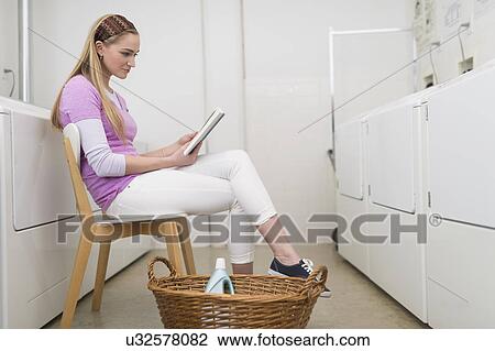 Stock Image - Woman reading book in laundromat. Fotosearch