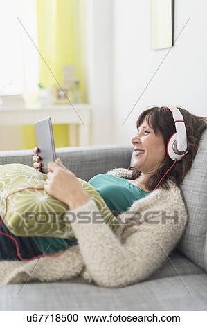 Woman relaxing on sofa, listening to music on tablet pc View Large Photo Image Stock Image - Woman relaxing on sofa, listening to music on tablet pc. Fotosearch