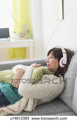 Stock Image - Woman relaxing on sofa, listening to music. Fotosearch