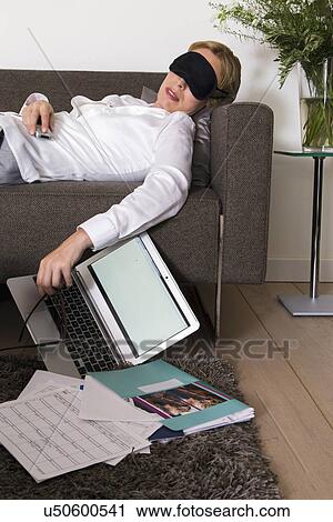Stock Image - Woman sleeping on sofa while working at home. Fotosearch