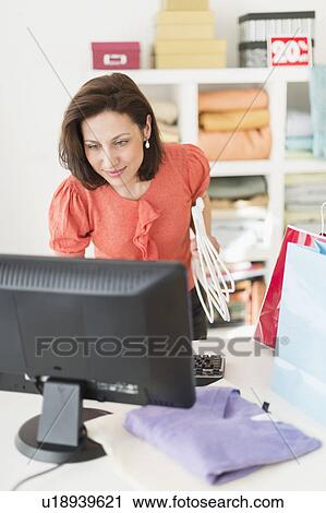 Stock Image - Woman using computer in clothes store. Fotosearch