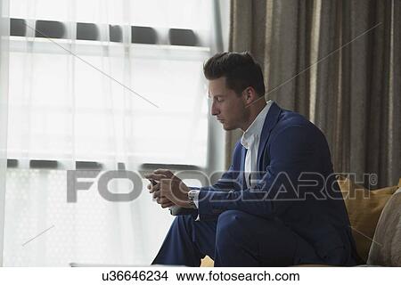 Young businessman sitting inside and text messaging View Large Photo Image Picture - Young businessman sitting inside and text messaging. Fotosearch