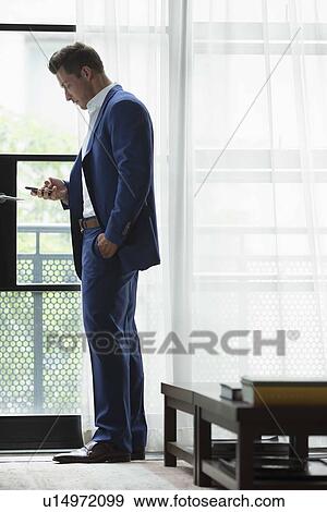 Young businessman standing inside and text messaging View Large Photo Image Stock Photo - Young businessman standing inside and text messaging. Fotosearch