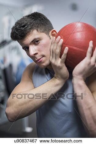Stock Photo - Young man at gym holding medicine ball. Fotosearch