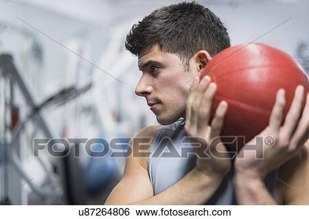 Stock Photograph - Young man at gym holding medicine ball. Fotosearch