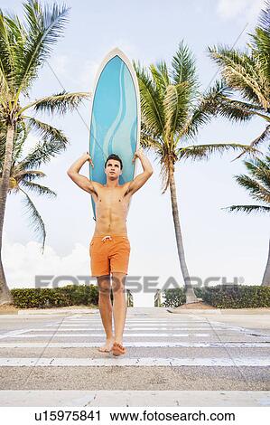 Young man carrying surfboard View Large Photo Image Stock Image - Young man carrying surfboard. Fotosearch