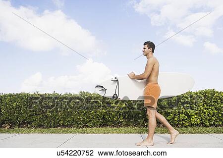 Young man carrying surfboard View Large Photo Image Stock Image - Young man carrying surfboard. Fotosearch