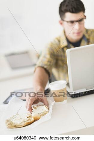 Young man eating sandwich and using laptop View Large Photo Image Stock Image - Young man eating sandwich and using laptop. Fotosearch
