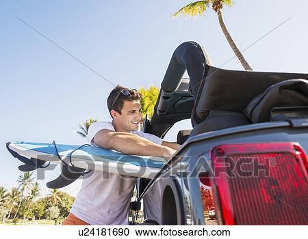 Stock Image - Young man packing surfboard. Fotosearch