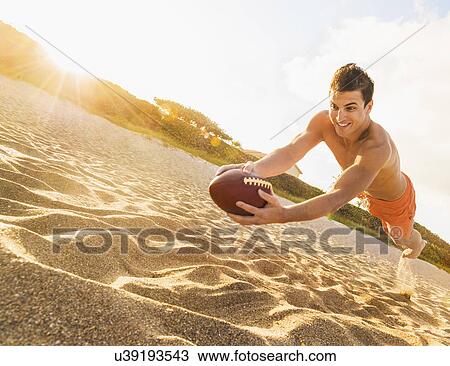 Stock Image - Young man playing football on beach. Fotosearch